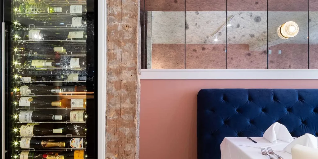 Restaurant interior with wine cooler, velvet booth, set table, mirrored panels.