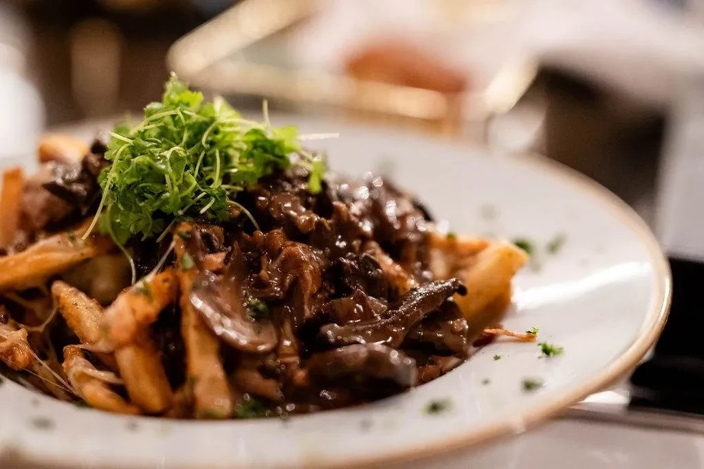 Poutine-style dish: fries, dark gravy, mushrooms, and fresh green herbs.