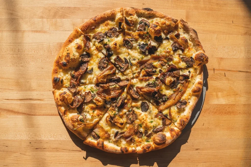 Freshly baked mushroom pizza with white sauce on a wooden table.