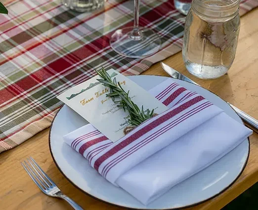Place setting on plaid tablecloth with 'Farm Table Day' card and rosemary.