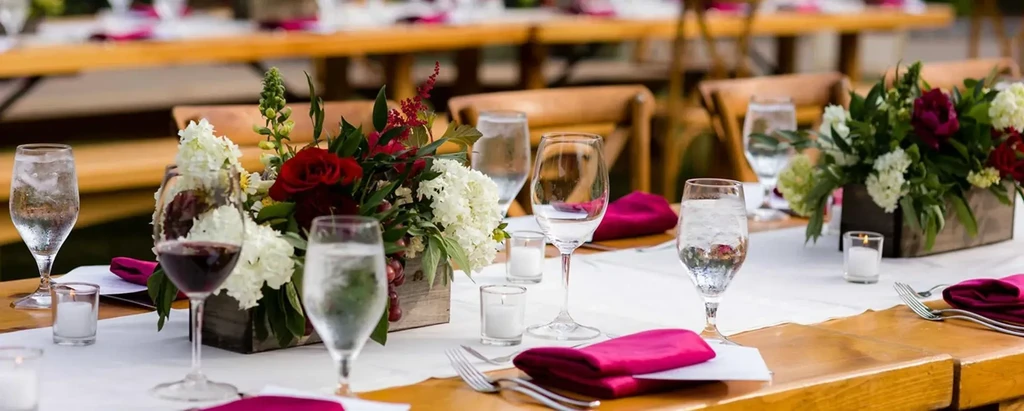 Elegant long dining table with flowers, pink napkins, wine, and candles.