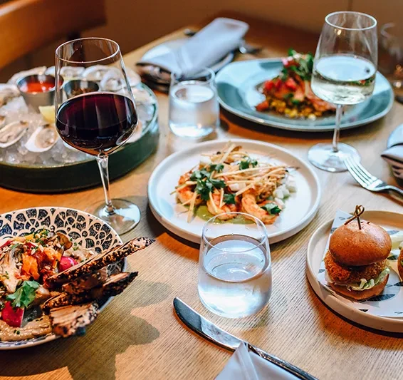 Table with oysters, shrimp, salad, slider, and glasses of wine.