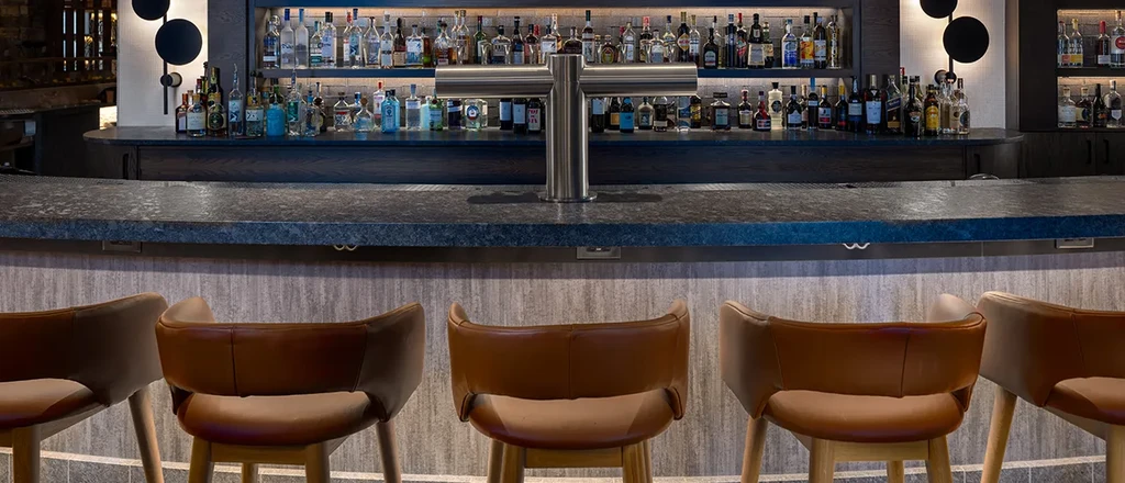 Modern bar area with leather stools and backlit liquor shelves.