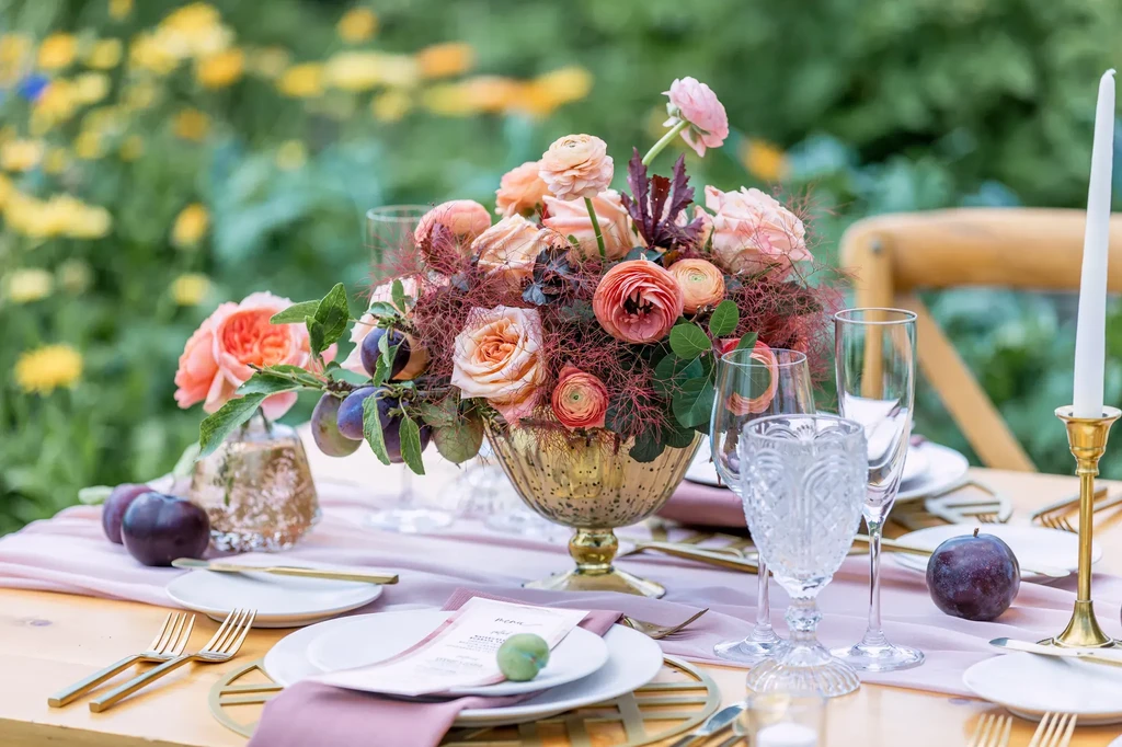 Lavish pink floral centerpiece and plums on an elegant outdoor dining table.