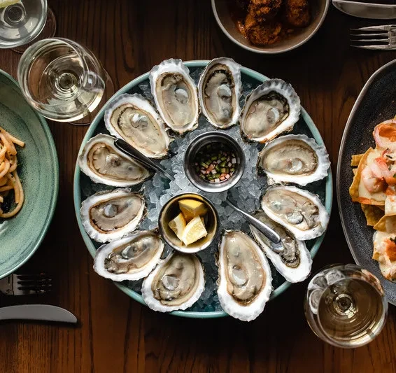 Overhead: Platter of fresh oysters with lemon, pasta, and seafood dishes.