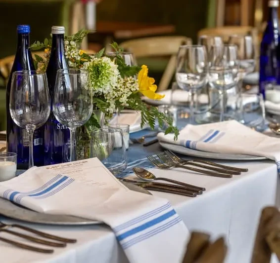 Dining table with blue runner, silver chargers, Guest Chef menu, San Pellegrino.