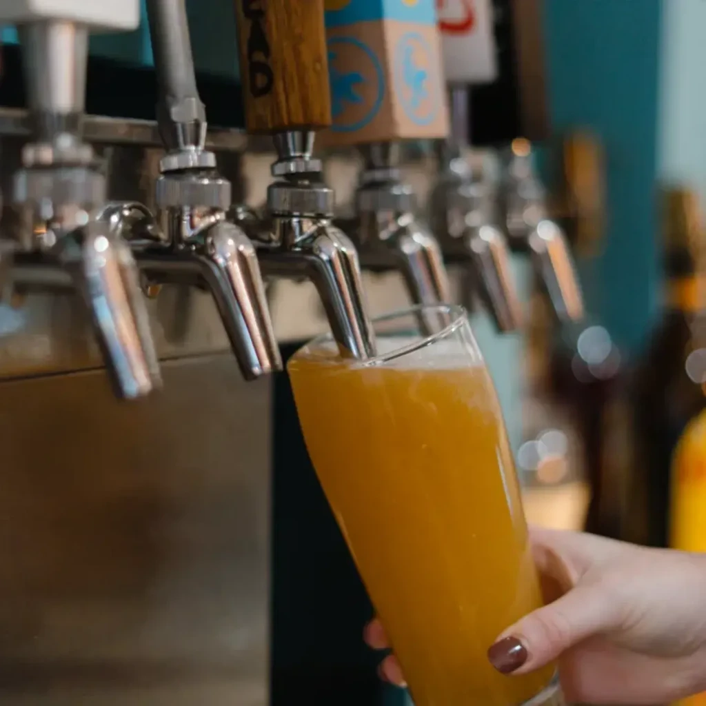 Hand holds glass filling with golden beer from bar tap.