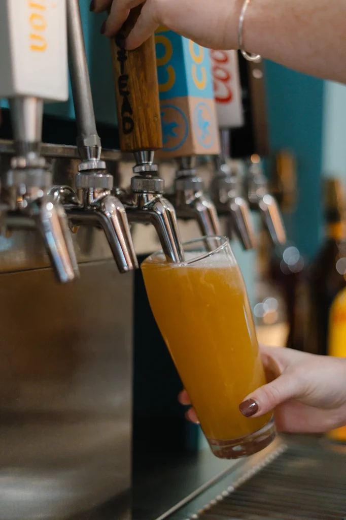 Hand pouring golden foamy beer from a tap into a glass.