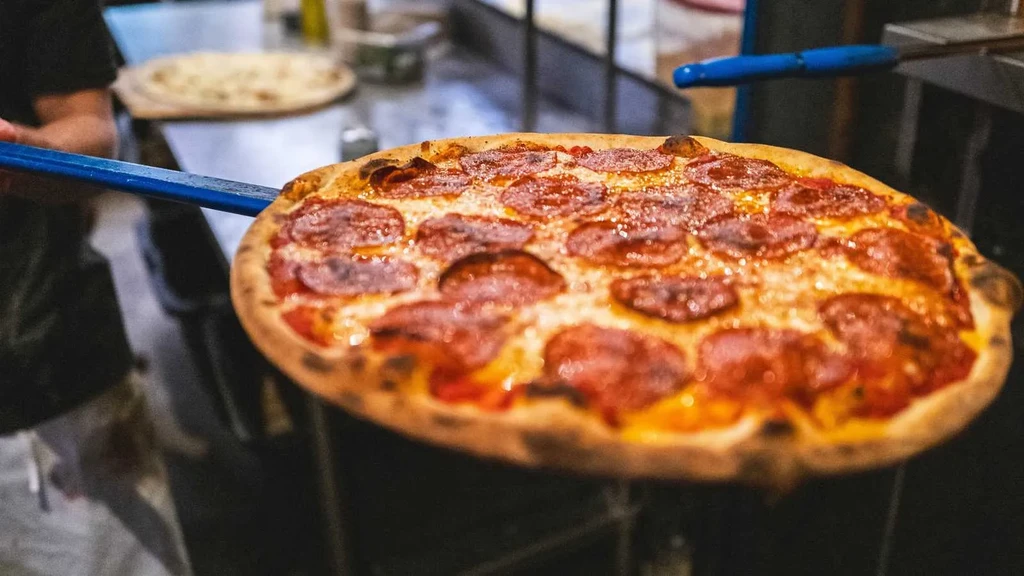 Person holding freshly baked pepperoni pizza on a blue peel.