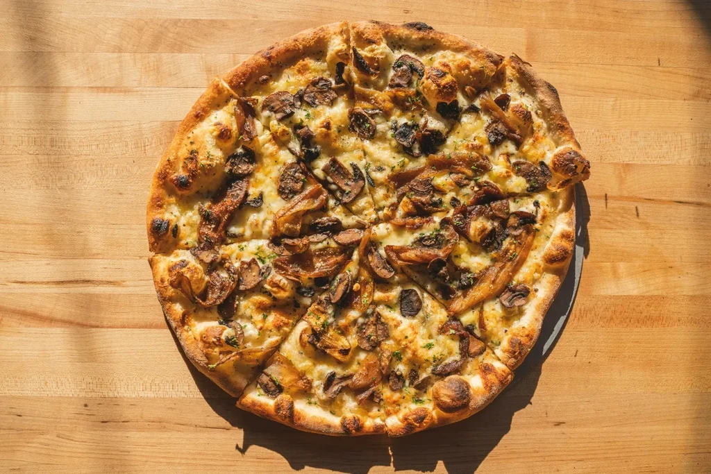 Eight-slice mushroom pizza with melted cheese and green herbs on wood.