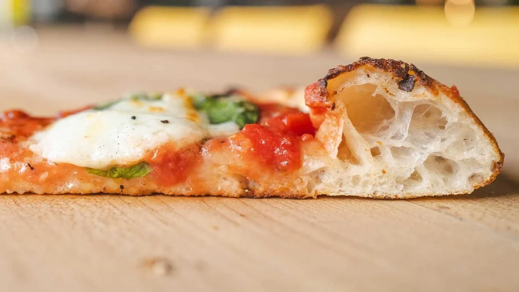 Close-up side-profile of a Neapolitan pizza slice with mozzarella and basil.