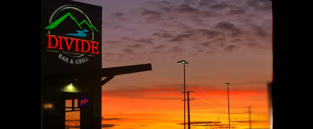 Divide Bar & Grill exterior, 'OPEN' sign, vibrant sunset sky.