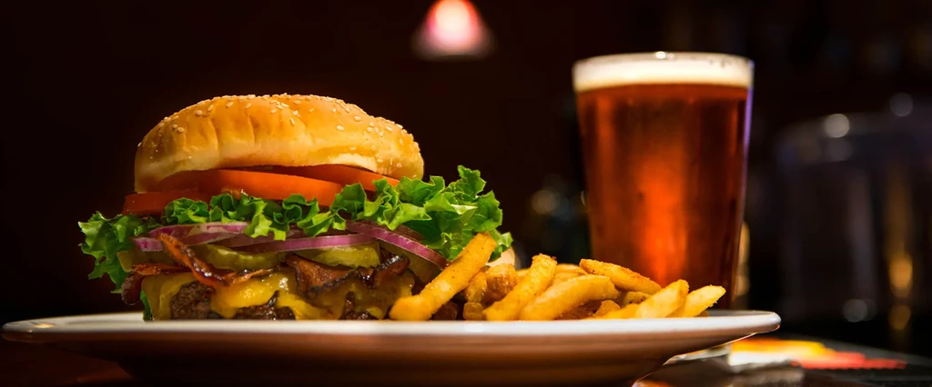A burger and fries with amber beer on a plate.
