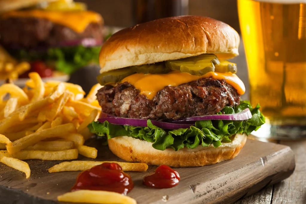 Gourmet cheeseburger, golden fries, ketchup, and beer on a wooden board.
