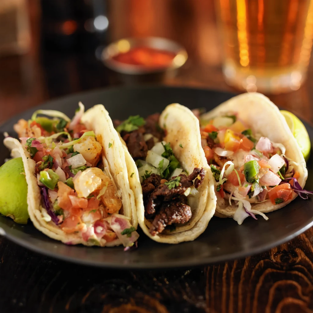 Three colorful tacos with shrimp, beef, pico de gallo, and lime.