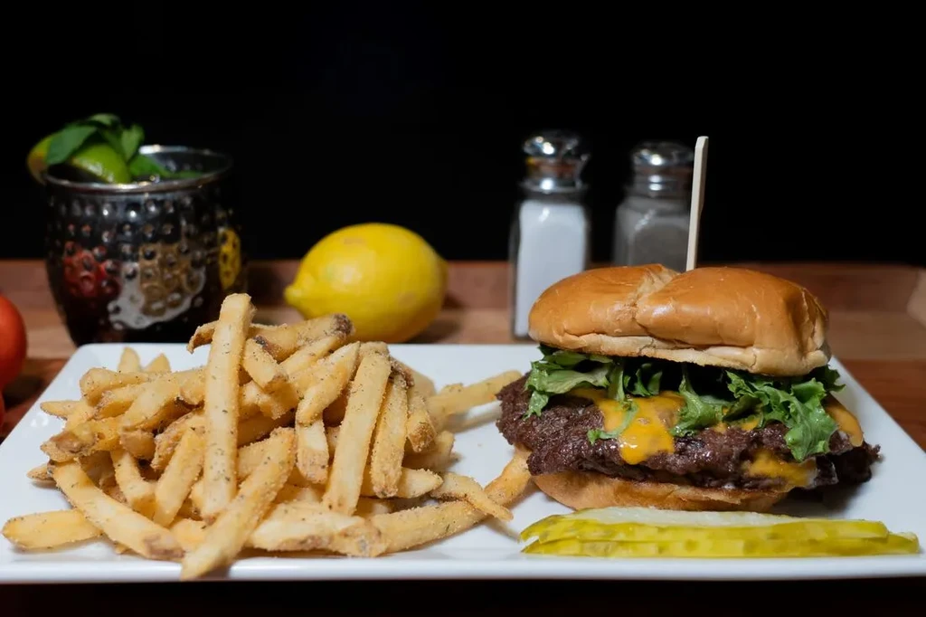 Double cheeseburger, seasoned fries, pickle, and garnished drink on a plate.