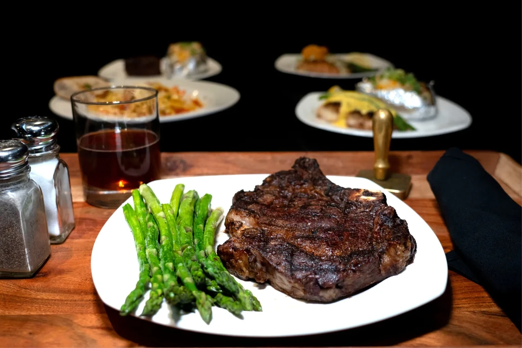 Seared steak, green asparagus, and amber drink on a wooden table.