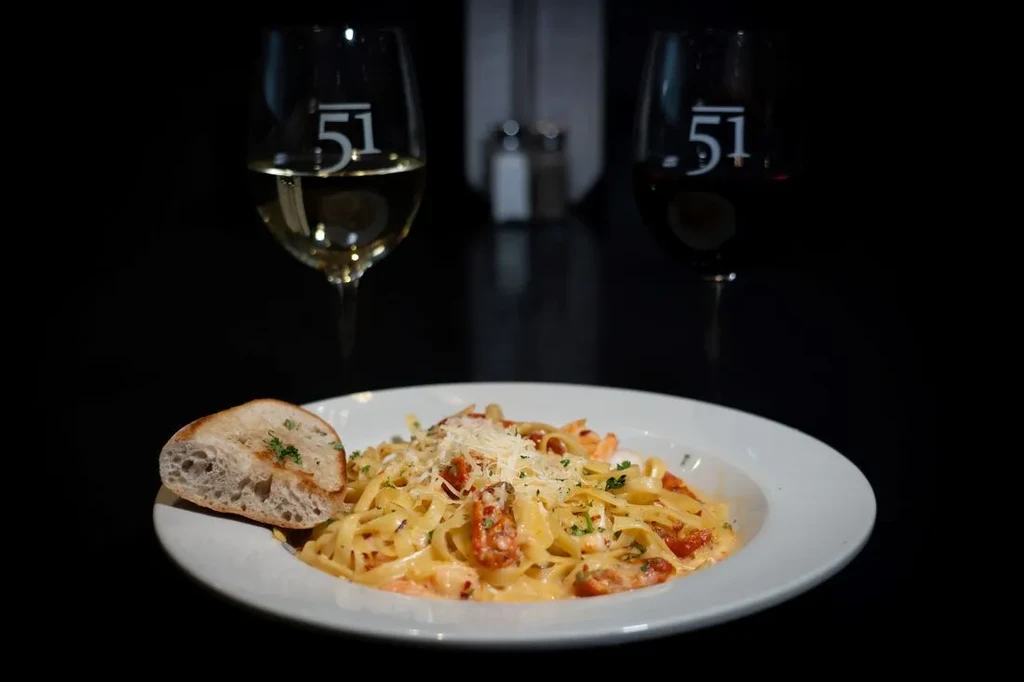 Creamy shrimp pasta with sun-dried tomatoes, bread, and wine glasses.