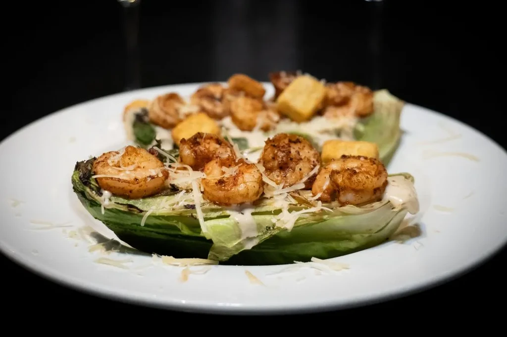 Plated grilled romaine Caesar salad with shrimp and croutons.