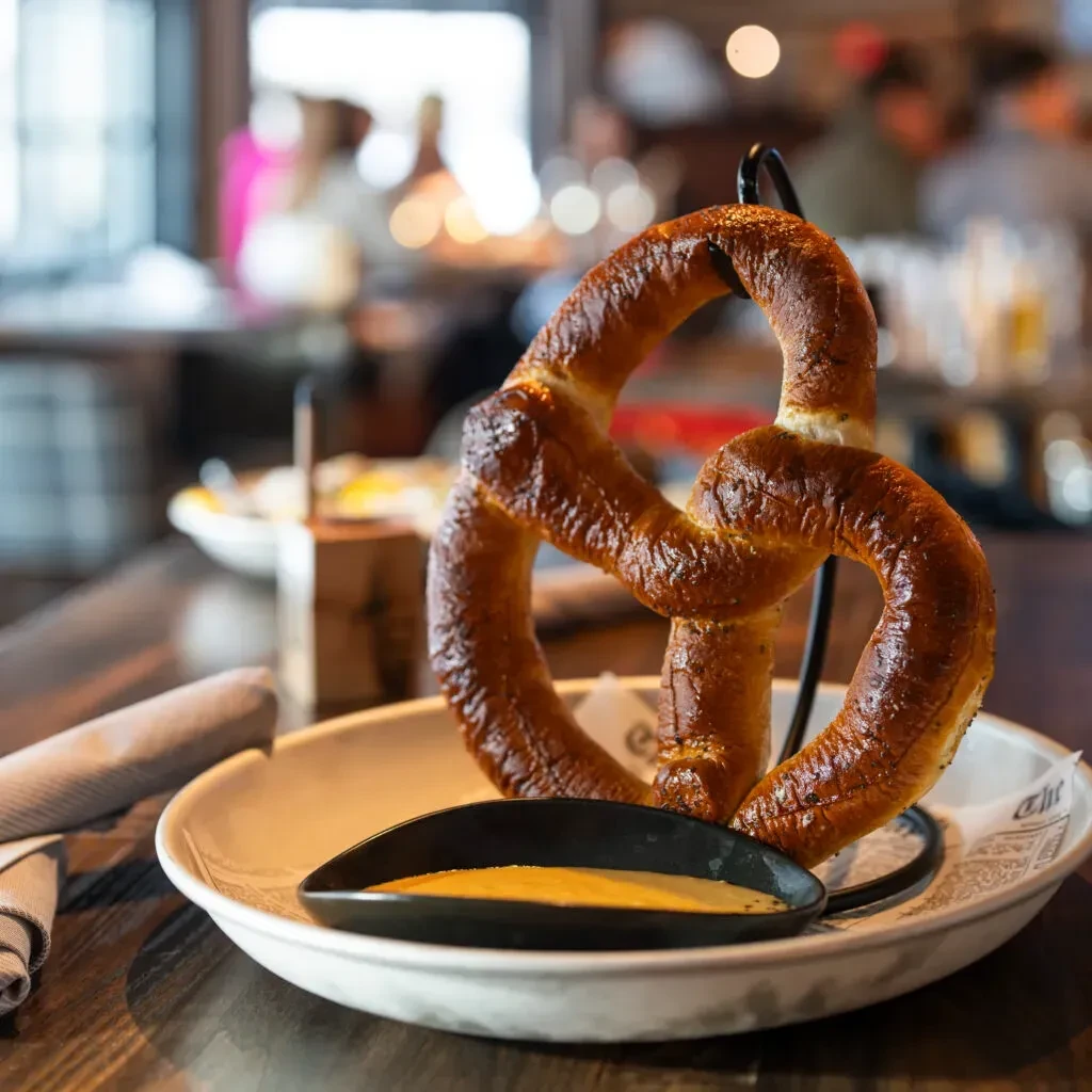 Large golden-brown pretzel, dipping sauce, and napkin on a wooden table.