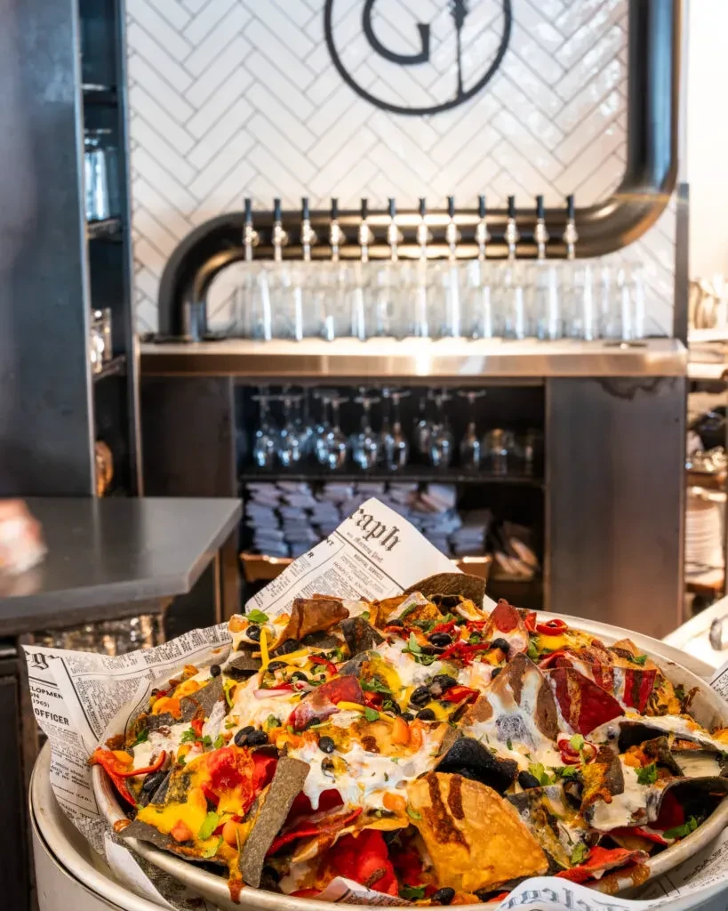 Overflowing nachos with diverse toppings in a bar setting.