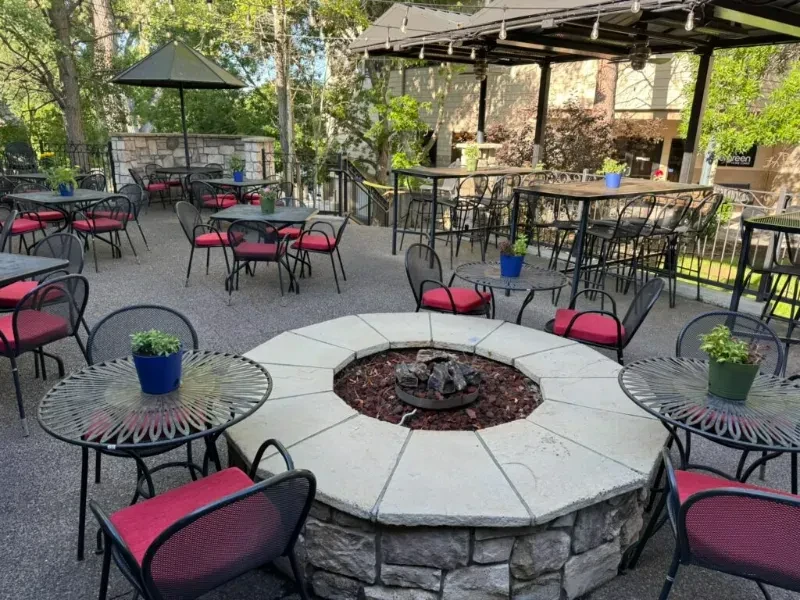 Outdoor restaurant patio with stone fire pit, tables, and pergola bar.