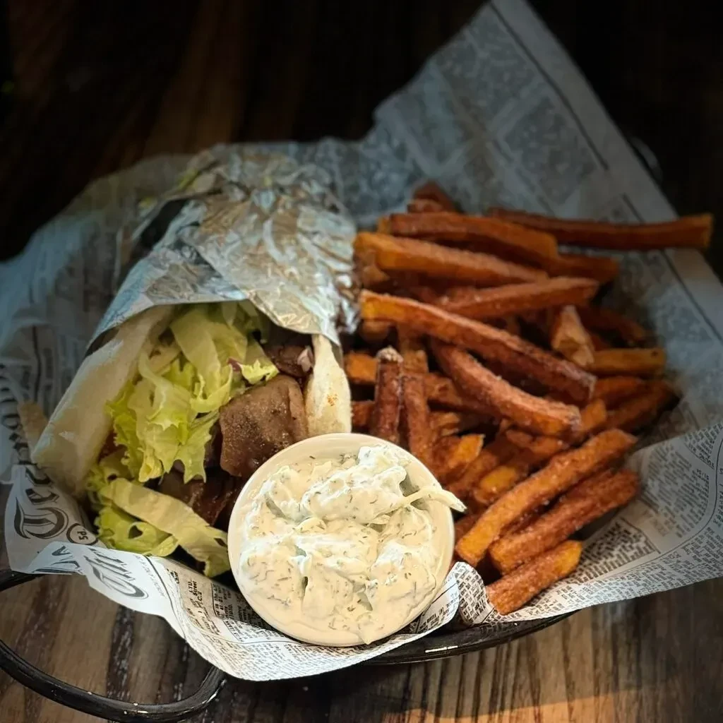 Top-down view: Gyro, sweet potato fries, tzatziki in newspaper-lined basket.