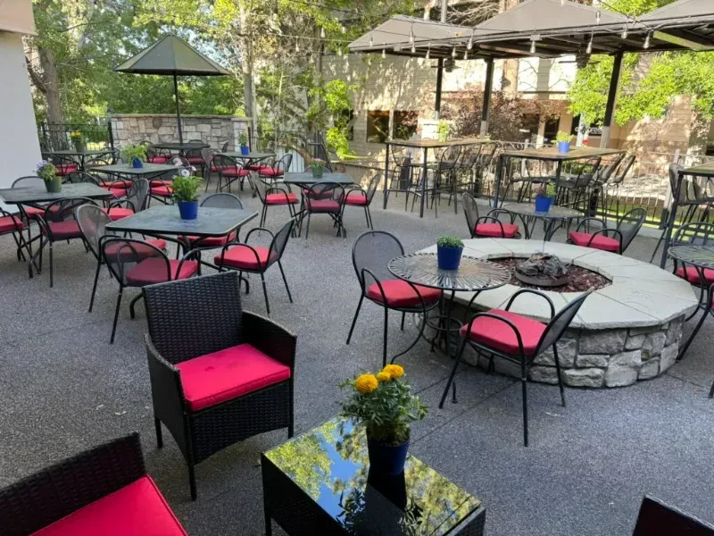 Empty outdoor patio with tables, chairs, fire pit, and red cushions.