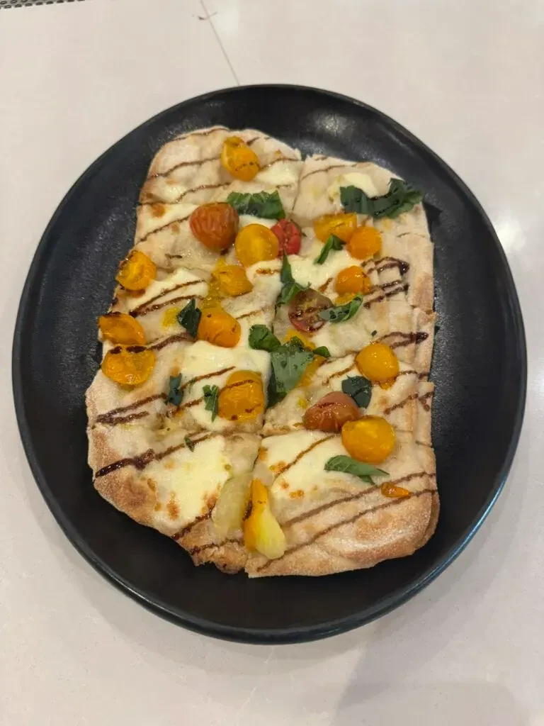 Grilled flatbread pizza with cheese, cherry tomatoes, basil, and balsamic.