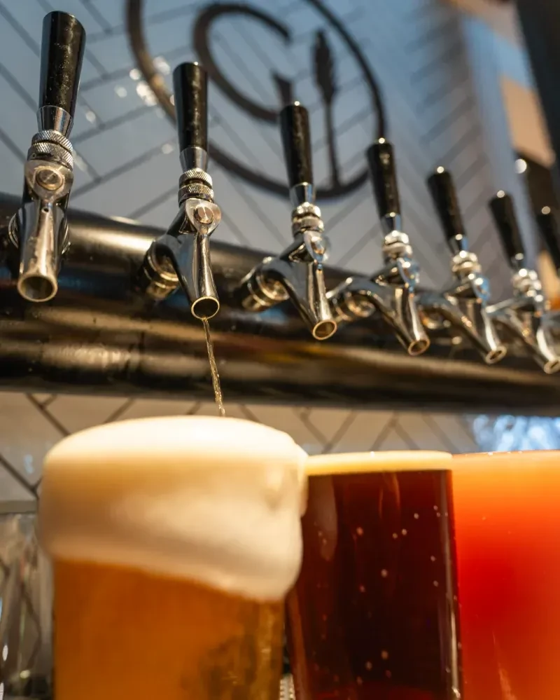 Beer taps pouring three different beverages, one overflowing with foam.