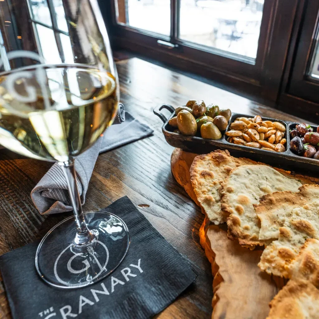 White wine, appetizer spread, and snowy background on wooden table.