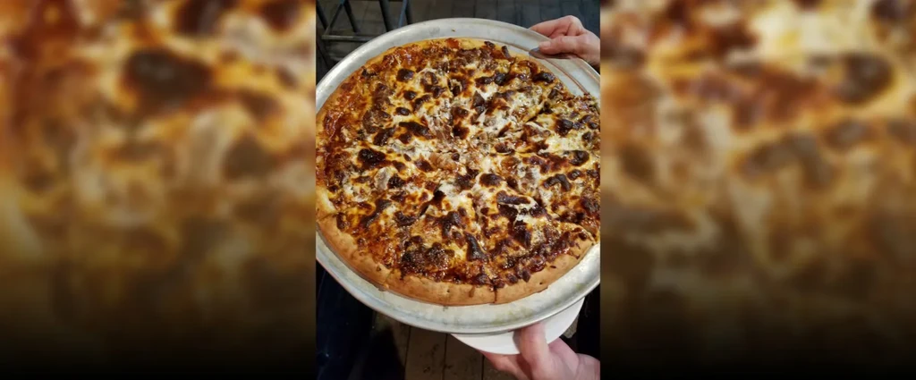 Hands holding a freshly baked pizza with dark, caramelized toppings.