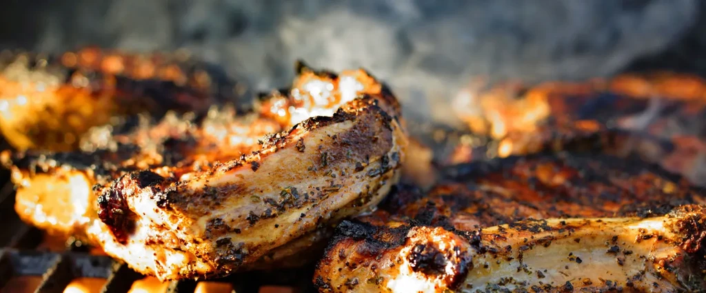 Close-up of seasoned meat grilling on a smoky barbecue.