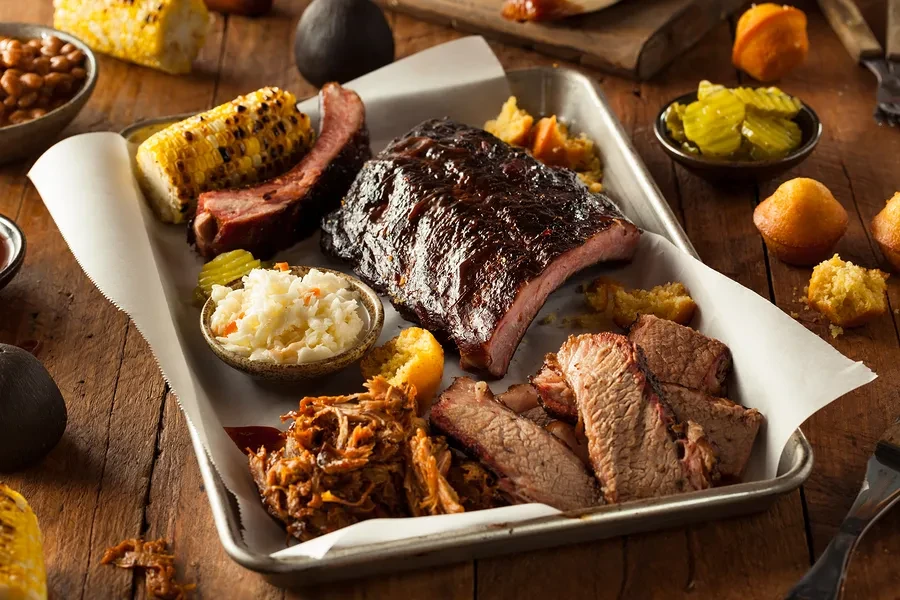 Barbecue platter: ribs, brisket, pulled pork, corn, coleslaw, muffins.