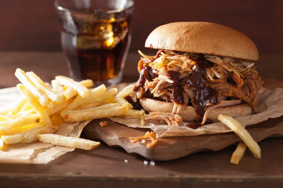 Pulled pork sandwich with coleslaw, fries, and an iced drink.