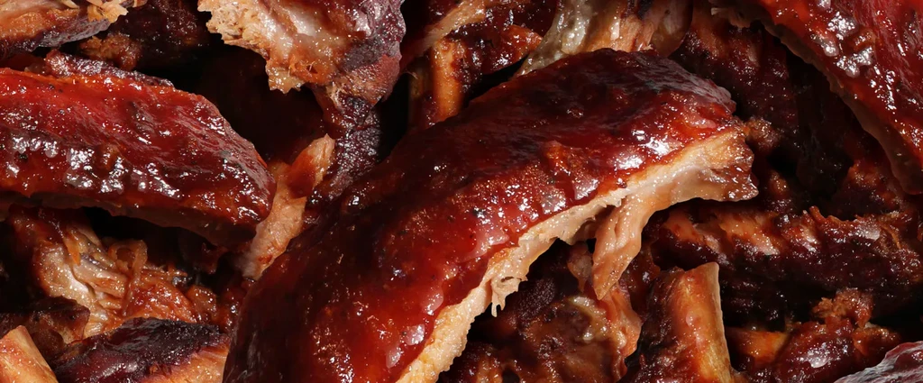 Piled, tender BBQ ribs with glistening reddish-brown sauce.
