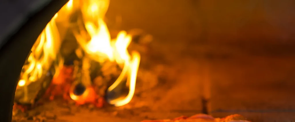 Close-up of wood-fired pizza oven with intense flames baking pizza.