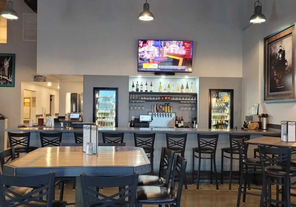 Empty modern bar and restaurant with lit bar, stools, and TV.