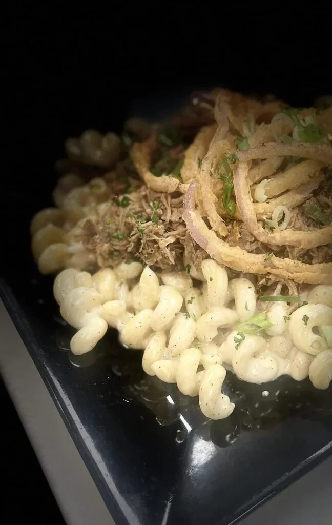 Macaroni and cheese topped with pulled meat and crispy onion rings.