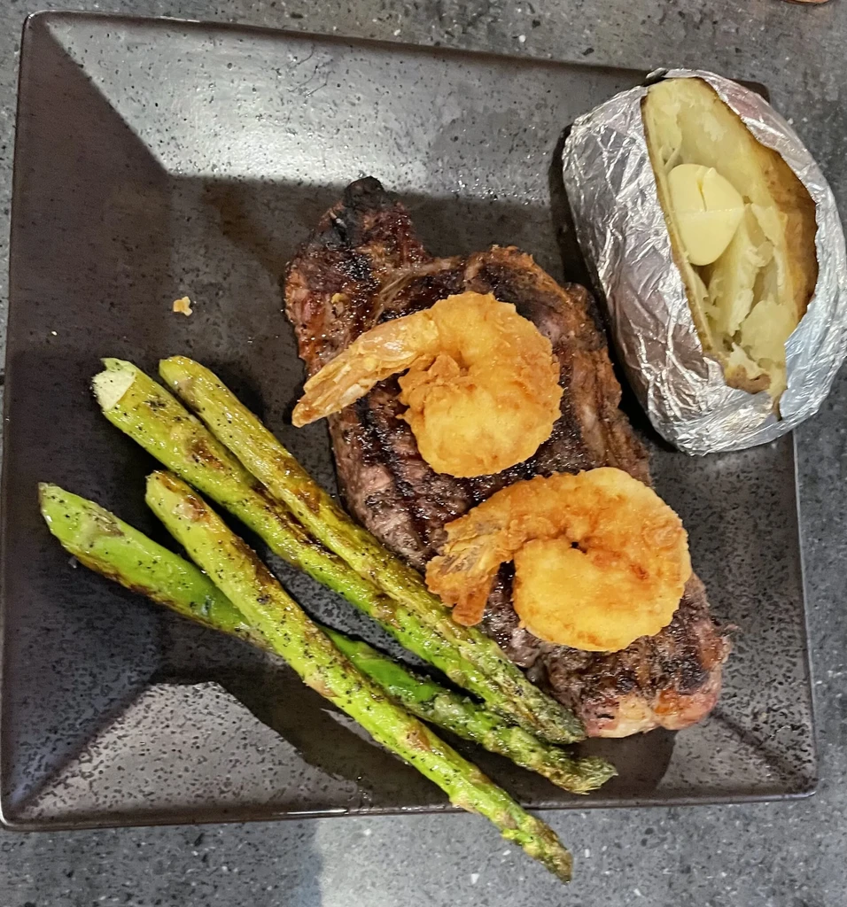 Overhead view of grilled steak, fried shrimp, asparagus, and buttered baked potato.