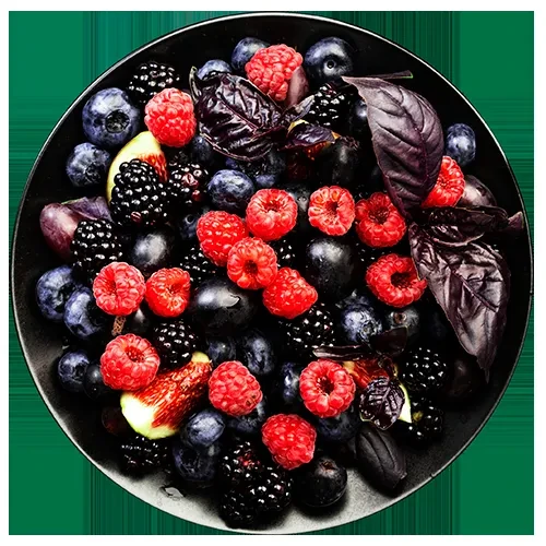 Dark bowl brimming with fresh berries, purple leaves, and sliced dark fruit.
