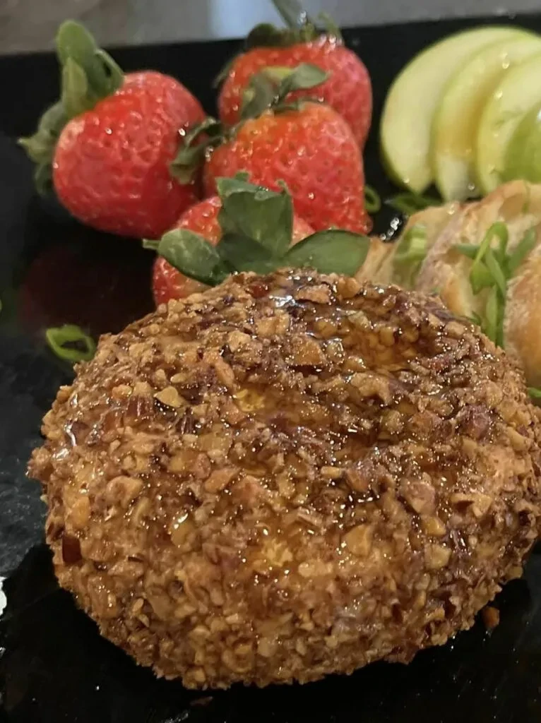Golden-brown, nut-crusted dish with syrup, strawberries, apples, and bread.