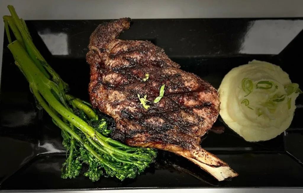Plated grilled steak, broccolini, mashed potatoes on a black plate.