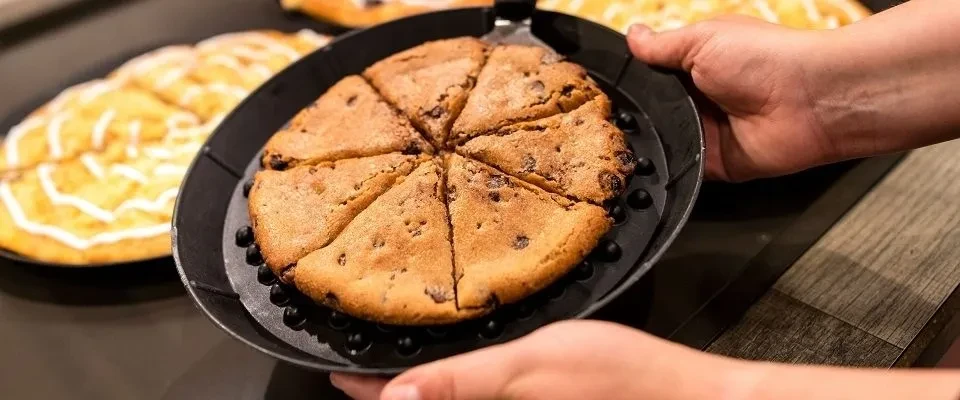 Sliced chocolate chip cookie in black pan, held by hands.