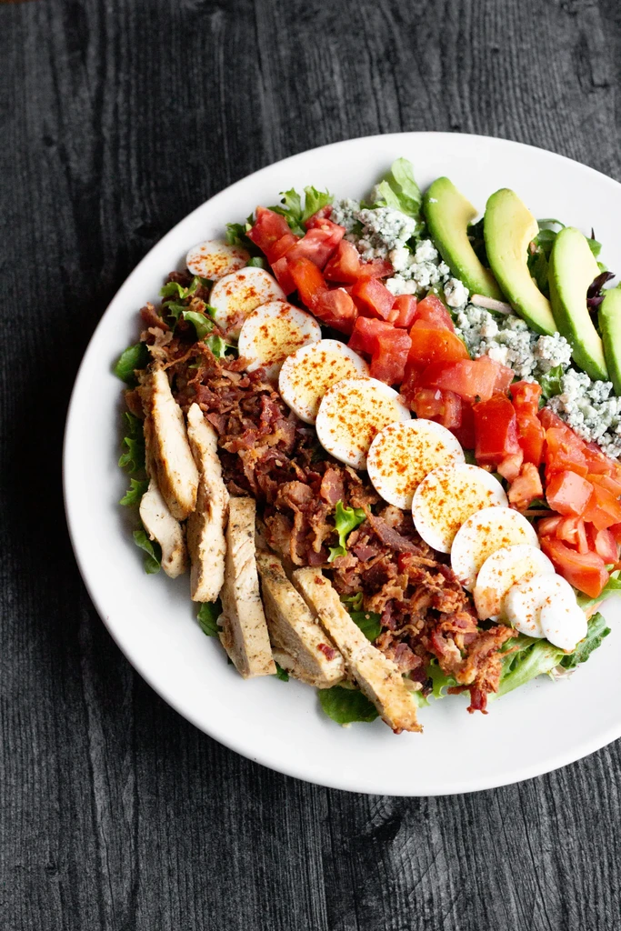 Colorful salad with grilled chicken, bacon, eggs, blue cheese, and avocado.