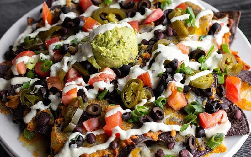 Blue corn nachos piled high with cheese, guacamole, beans, and vegetables.
