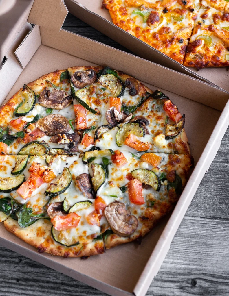 Two sliced takeout pizzas, one vegetarian, on a wooden surface.