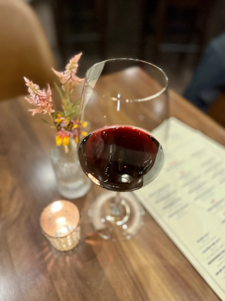 Glass of red wine, flowers, and lit candle on a wooden table.