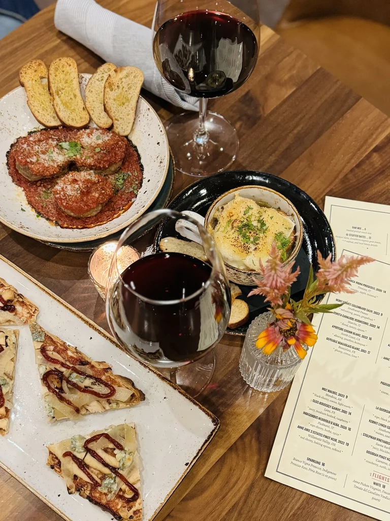 Dining table with diverse dishes, red wine, flowers, and a menu.