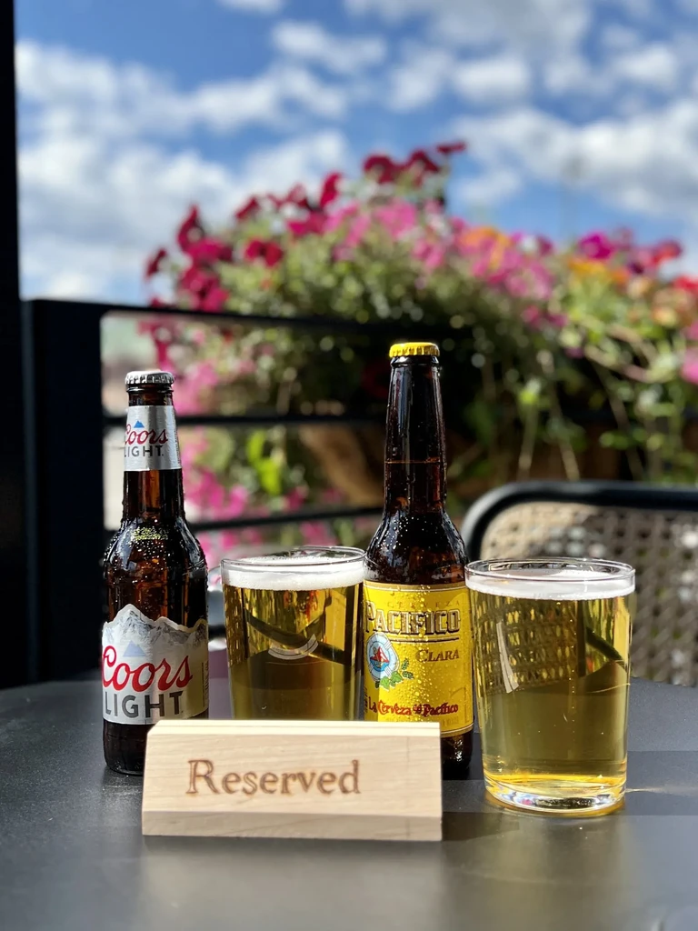 Two cold beers, glasses, and a 'Reserved' sign on an outdoor table.